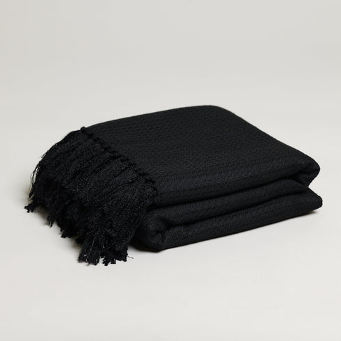 large soft textured black throw blanket folded up with tassels