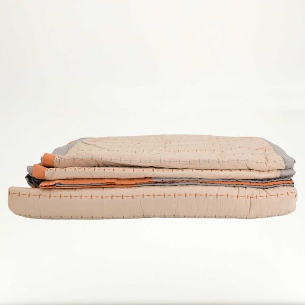 Folded tan bed set with a white background with an orange and grey rim