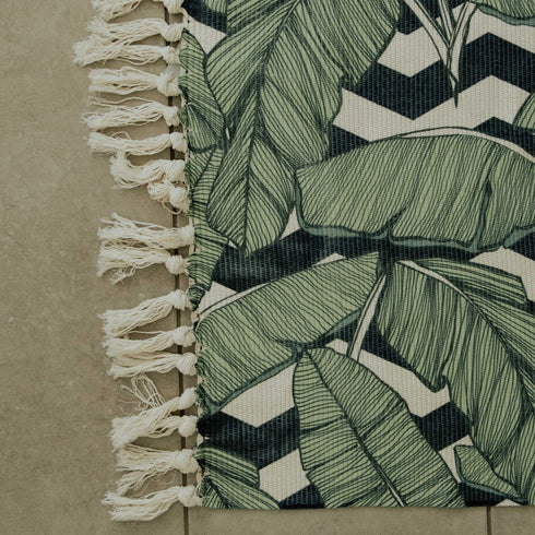 leaf design rug mat with white tassels on it with black and white geometric pattern behind it